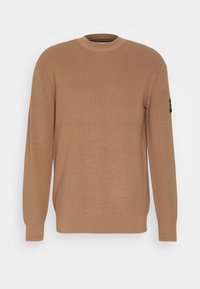 Brązowy sweter o plecionym wzorze, z okrągłym dekoltem, długimi rękawami, ryflowanym wykończeniem oraz małą naszywką z logo na prawym rękawie.