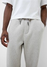 Graue Baumwoll-Sweatpants mit einem elastischen Bund, Kordelzugverschluss, seitlichen Taschen und einer lockeren Passform. Weicher Stoff, minimalistisches Design.