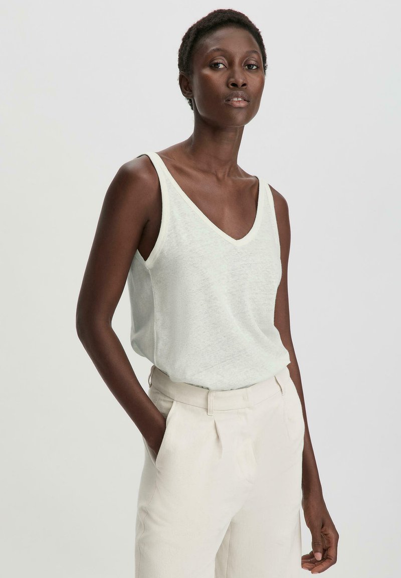 Vaaleanvihreä, hihaton V-päätä yläosa, joka on valmistettu pehmeästä kankaasta, yhdistettynä kermaisiin housuihin. Tasainen rakenne, rento istuvuus.