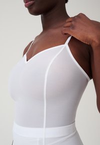 Witte tanktop met dunne bandjes, v-hals en een gladde textuur. Getailleerd ontwerp met subtiele naden en een contrasterende rand.