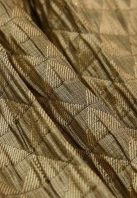 Gequiltes Material in Gold- und Schwarztönen mit einem geometrischen Muster. Die Textur ist glatt mit einem dezenten Glanz und zeigt filigrane Nähte.