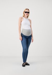 Kismama öltözet, amely tartalmaz egy testhez simuló fehér trikót, szürke, a pocakra tépődő derékpántot, kék skinny farmert és fekete lapos cipőket. Simább anyagok.