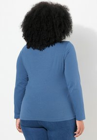 Langsleeve blauwe top van zacht materiaal, met een afgeronde zoom en aansluitende pasvorm, gecombineerd met donkere denim jeans.