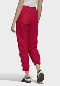 Červené, lehké, elastické tepláky v pase s bílými bočními pruhy a zúženými manžetami, doplněné o černobílé tenisky.