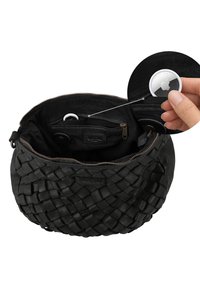 Schwarze gewebte Lederhandtasche geöffnet, um eine innere Reißverschlusstasche zu zeigen, wobei eine Hand einen weißen Apple AirTag nahe der Tasche hält.