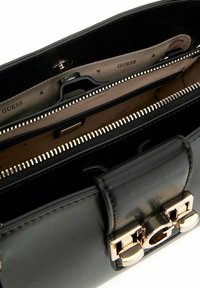 Sac à main en cuir noir avec un fermoir en métal doré, des compartiments zippés et un intérieur beige avec un motif de logo.