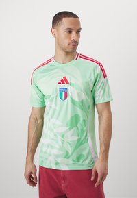 Žalias sportinis marškinėlis su lapų raštu, raudoni akcentai ant pečių ir centrinis "Italia" herbas. Trumpomis rankovėmis ir apykaklės dizainas.