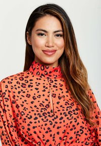 Orange blouse with a high collar, featuring a black leopard print design. Smooth texture with a notch detail at the neck and flowing fit.
