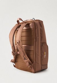 Barna párnázott hátizsák állítható pántokkal, hálós hátsó panellel, oldalsó zsebbel, amelyen a "Cordura Advanced Fabrics" felirat található, és egy felső hordozó fogantyúval.