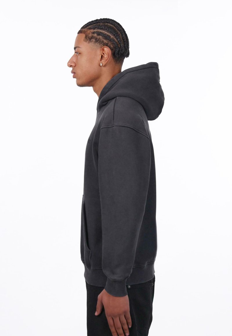 Pullover hoodie in donkergrijs, gemaakt van zachte stof; heeft een voorzak, ribgebreide manchetten en een capuchon met trekkoord. De zijaanzicht toont een slanke pasvorm.