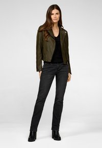 Olivengrøn læderjakke med en tætsiddende design, lynlåslommer og sølvhardware, parret med sort top og mørke jeans.