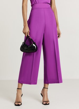 Pantalon large violet à taille haute avec des plis nets. Associé à un sac à main noir brillant et des talons noirs à brides.