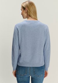 Jasnoniebieski sweter z dzianiny z okrągłym dekoltem, prążkowanymi mankietami i dołem. Posiada miękką teksturę oraz rękawy raglanowe, zestawiony z dopasowanymi dżinsami.