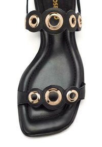 Sandalo nero con design a punta quadrata, texture in morbida pelle e tre accenti circolari oro sulle cinghie.