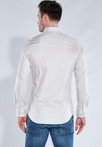 Weißes Langarmhemd mit klassischem Kragen, glatter Textur, Knopfmanschetten und taillierter Passform, kombiniert mit blauen Jeans.