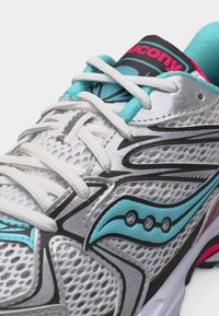 Αθλητικό παπούτσι τρεξίματος Saucony σε λευκό και πράσινο-μπλε με επάνω μέρος από δίχτυ, λευκά κορδόνια και μαύρο-ροζ λογότυπο στη γλώσσα, σε λευκό φόντο.