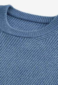 Primo piano di un maglione blu lavorato a maglia, caratterizzato da una trama a coste e un collo rotondo. Il tessuto mostra variazioni di tonalità.