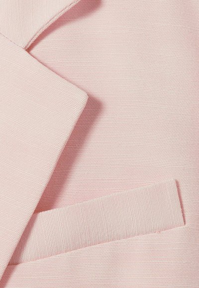 Tissu texturé rose pâle avec un revers plié et un rabat de poche horizontal, mettant en valeur les détails et la texture du vêtement.