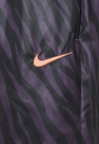 Tessuto nero e viola con un motivo a strisce di tigre, con un logo Nike ricamato arancione su un lato. Texture morbida con una finitura liscia.