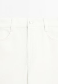 Close-up of white denim jeans waist with button closure, belt loops, and front pockets.