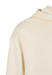 Gros plan sur l'épaule et la couture de la capuche d'un sweat à capuche en tissu beige avec une texture douce et une finition lisse.