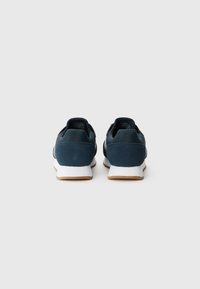Donkerblauwe suède en synthetische sneakers met een witte middenzool en een gumrubberen zool. Kenmerken zijn de afgeronde vorm en de gevoerde kraag.
