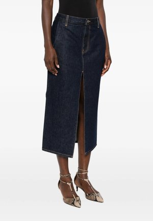 Donna che indossa una gonna midi di denim blu scuro con spacco frontale, abbinata a scarpe con tacco alto e cinturino alla caviglia con stampa serpente e un top nero.