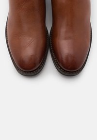 Botas de cuero marrón con un acabado suave, punteras redondeadas y costuras en contraste a lo largo de la suela. Suela plana y duradera para mayor estabilidad.