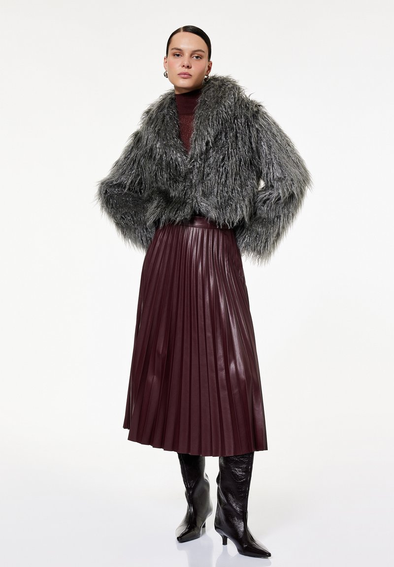 Grå faux fur cropped jakke, bordeaux plisseret nederdel og glansfulde sorte knæhøje støvler. Slanke og strukturerede designelementer.