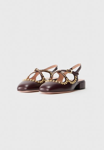 Scarpe slingback in pelle marrone con borchie dorate, caratterizzate da un design a taglio e tacco a blocco basso. Texture liscia e punta arrotondata.