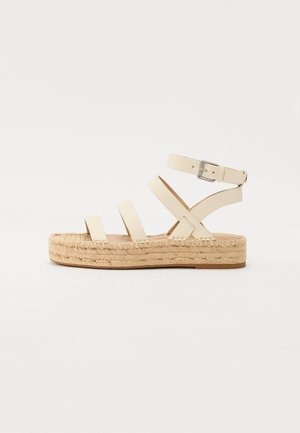 Sandalo platform beige con tre cinturini anteriori e cinghia alla caviglia con fibbia argentata su suola in juta intrecciata su sfondo bianco.