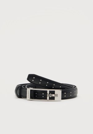 Ceinture en cuir noir avec petits clous argentés, roulée avec une boucle rectangulaire argentée sur un fond clair uni.