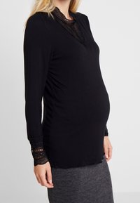 Svart långärmad topp med spetsdetaljer vid kragen och ärmsluten, figurnära design, mjukt material, lämplig för gravidkläder.