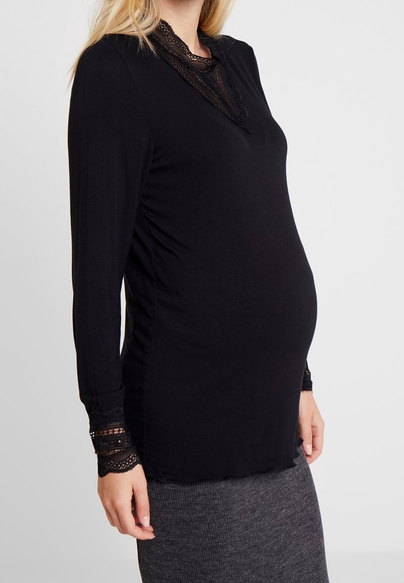 Svart långärmad topp med spetsdetaljer vid kragen och ärmsluten, figurnära design, mjukt material, lämplig för gravidkläder.