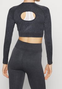 Dunkelgraues Cropped-Top mit langen Ärmeln, das einen runden Rückenausschnitt und gerippte Texturakzente aufweist. Kombiniert mit hochtaillierten Leggings.