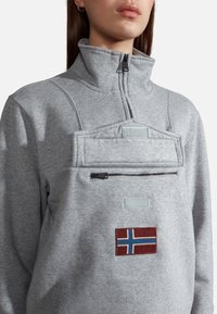 Fleece grigio con zip e colletto alto, dotato di tasca con zip e bandiera norvegese ricamata sul fronte, accentuato da patch in tessuto.