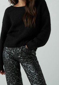 Pull en maille noire avec un col large et une coupe décontractée, associé à un pantalon en similicuir noir à motif léopard avec des poches latérales.
