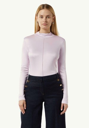 Hellblaues Langarmoberteil mit hohem Kragen, featuring einem Frontnahtdetail, kombiniert mit dunkelblauen weit geschnittenen Jeanshosen, akzentuiert mit goldenen Knöpfen.