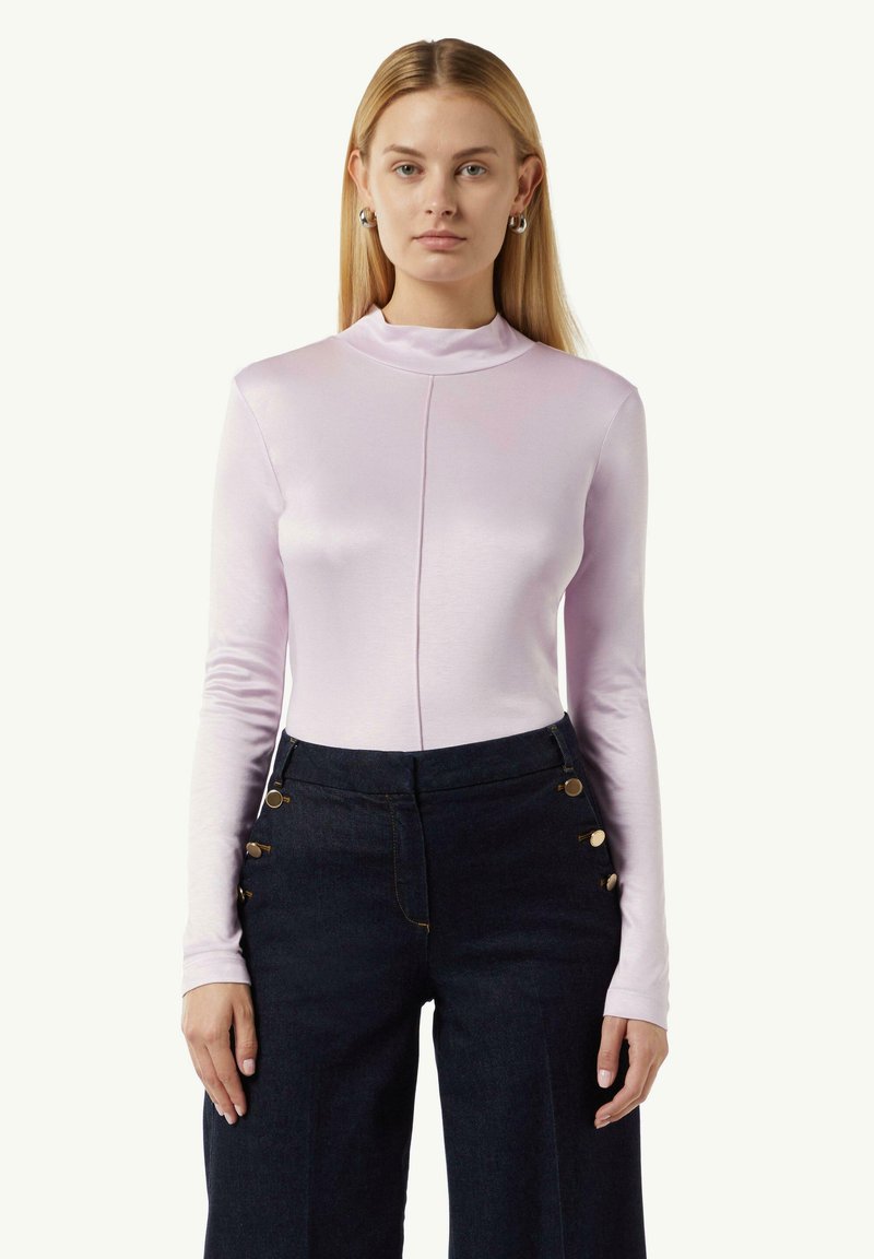 Hellblaues Langarmoberteil mit hohem Kragen, featuring einem Frontnahtdetail, kombiniert mit dunkelblauen weit geschnittenen Jeanshosen, akzentuiert mit goldenen Knöpfen.