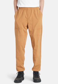 Tan cargobroeken met een elastische tailleband, voorzien van twee voorzakken en een losse pasvorm, gecombineerd met zwarte wandelschoenen.