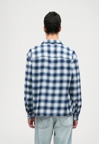 Πουκάμισο καρό σε μπλε και λευκό χρώ�μα από flannel, με μακριά μανίκια, γιακά και κουμπιά, παρουσιασμένο από πίσω σε μοντέλο που φοράει ανοιχτόχρωμα τζιν.