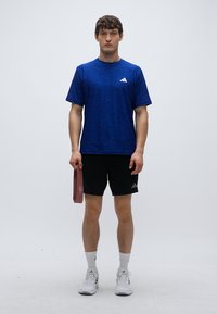 Modré športové tričko s textúrovaným vzorom, logo na hrudi; čierne šortky; drží bordovú odporovú pásku; biele ponožky a športová obuv.