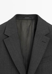 Dunkelgrauer maßgeschneiderter Blazer mit Revers, Innenfutter und einem "Made in Portugal"-Etikett im Kragen.