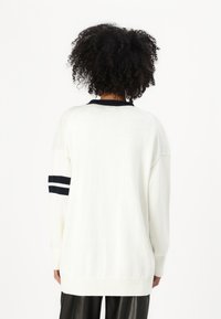 Weißer Strickpullover mit schwarzen Akzenten am Kragen und drei Streifen am Ärmel. Lässiger Schnitt und gerippte Bündchen.