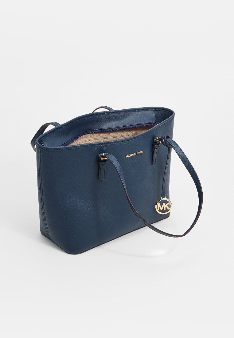 Grand sac fourre-tout en cuir bleu marine avec fermeture éclair, quincaillerie dorée, doubles poignées et breloque avec logo. Texture lisse avec un intérieur spacieux.