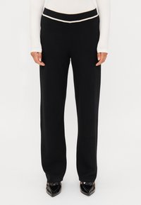 Černé kalhoty rovného střihu s vysokým pasem a kontrastním bílým lemem. Vyrobeny z měkké, elastické tkaniny.