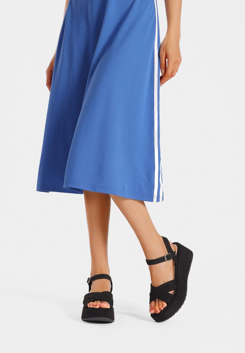 Sandali neri con piattaforma, cinturino alla caviglia regolabile, suola testurizzata e design open toe, abbinati a un vestito midi blu con strisce laterali bianche.