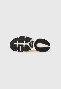 Sole de sneaker New Balance alb-negru, cu textură antiderapantă și logo în centru, pe un fundal gri deschis.
