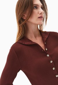 Ribbet bordeaux top med krave, med knaplukning foran og subtil tekstur, der fremhæver runde knapper og en tætsiddende pasform.