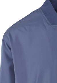 Chemise bleue à manches longues avec un col texturé et des coutures visibles le long de la couture de l'épaule et de la manche.